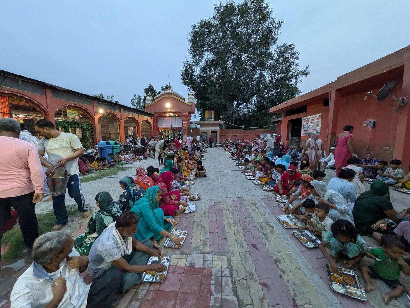 Devotees seated in rows for a community meal in the courtyard